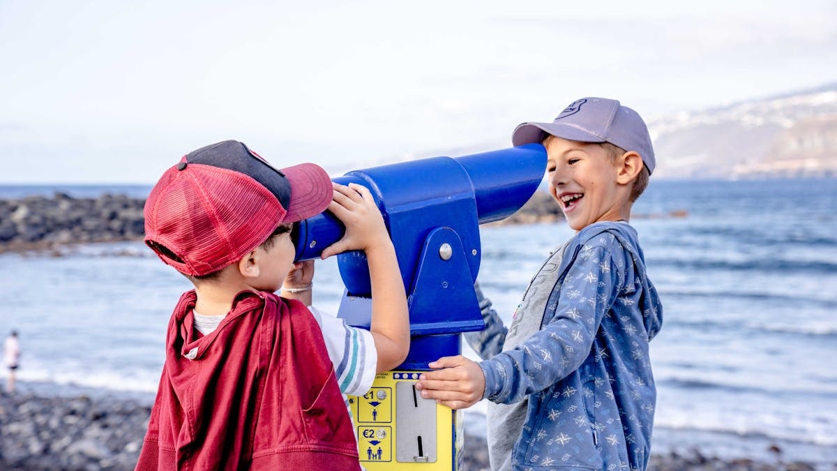 Two boys having fun with a telescope by the ocean in Puerto de la Cruz, Spain.